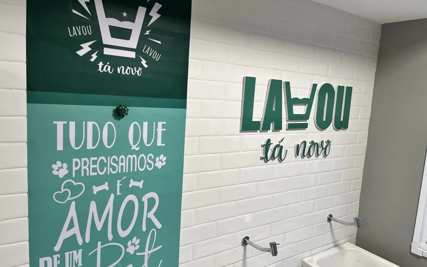 Parede de azulejos brancos com o logo da Lavou tá Novo e painel verde em uma lavanderia de condomínio